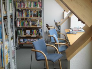 Bücherregale in der Stadtbücherei, davor zwei Stühle und ein Tisch am Fenster