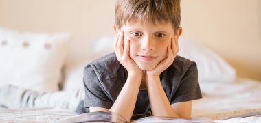 Junge liest auf dem Bett und scheint ganz gebannt von der Geschichte.