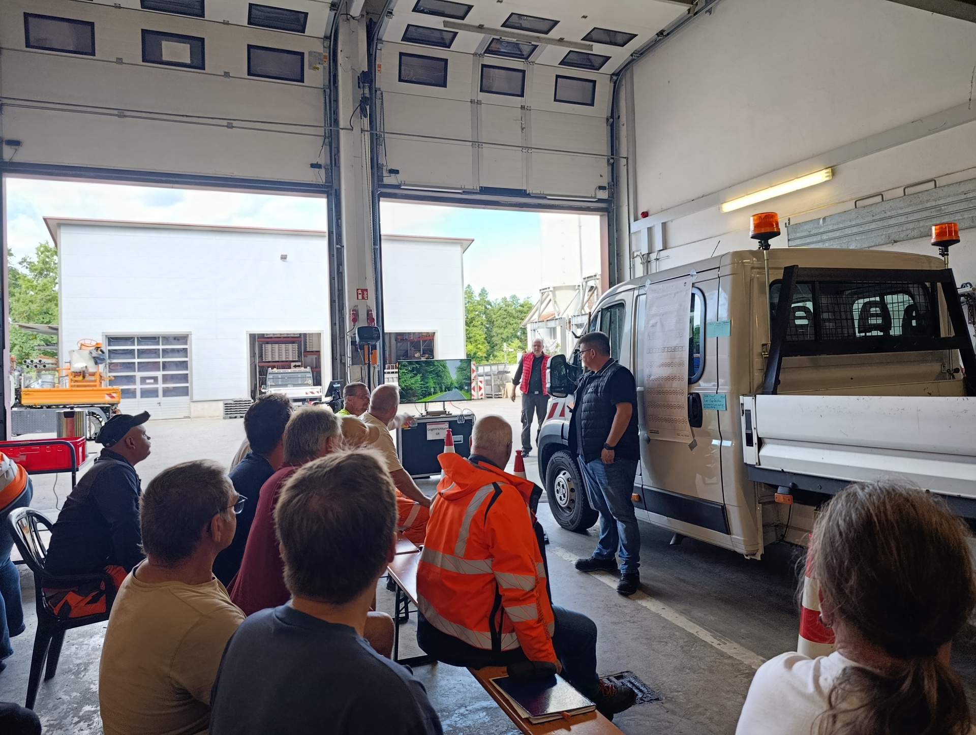 Bauhof-Mitarbeitende auf Bänken vor dem für die Schulung präparierten Kleinlaster in einer Halle am Bauhof Tettnang