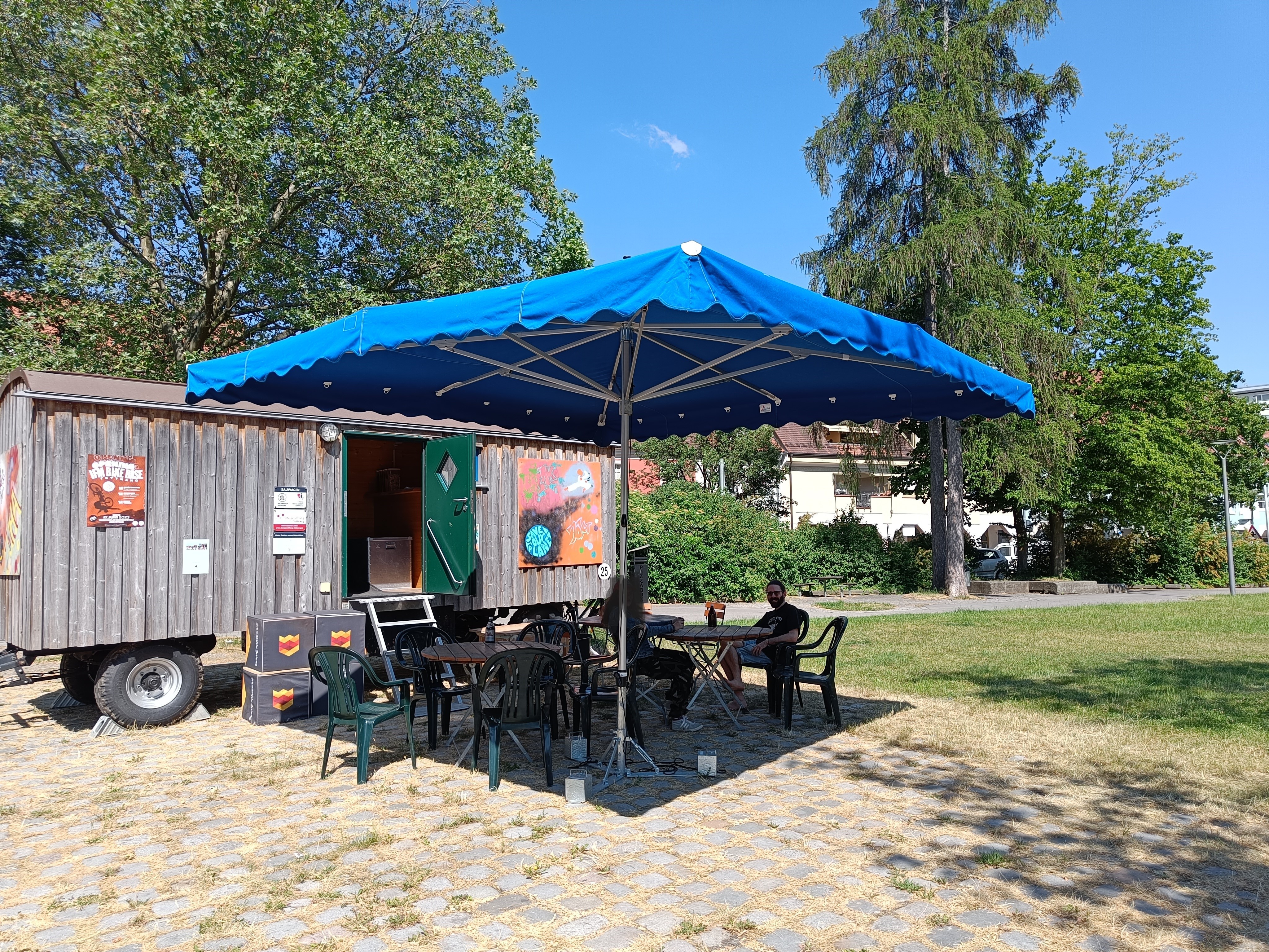 Bauwagen des Jugendhauses mit Sonnenschirmen und Sitzgelegenheiten davor