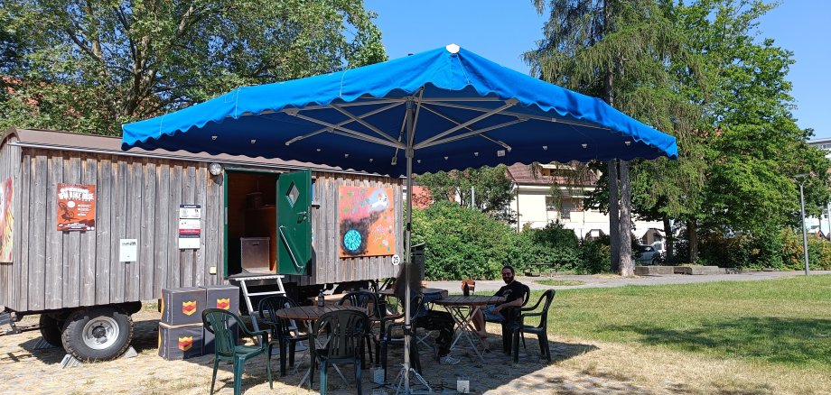 Bauwagen des Jugendhauses mit Sonnenschirmen und Sitzgelegenheiten davor