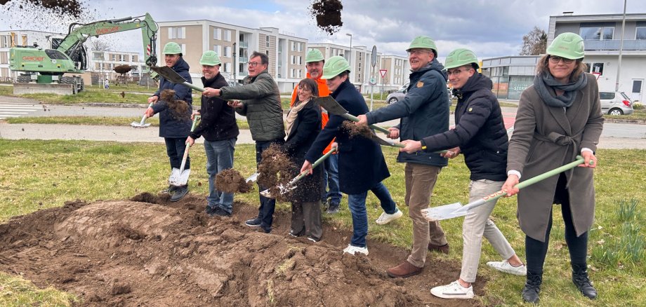 Acht Personen mit Spaten und Helmen nehmen den Spatenstich vor