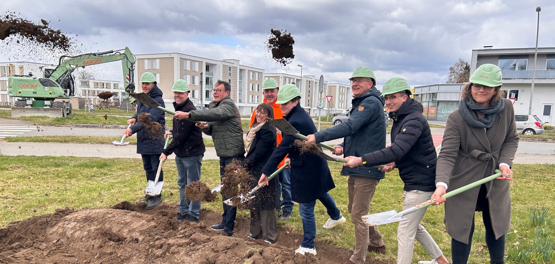 Acht Personen mit Spaten und Helmen nehmen den Spatenstich vor