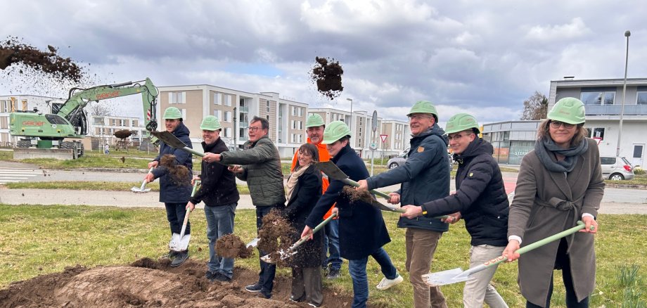 Acht Personen mit Spaten und Helmen nehmen den Spatenstich vor