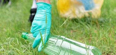 Hand hebt Plastikflasche vom Boden auf