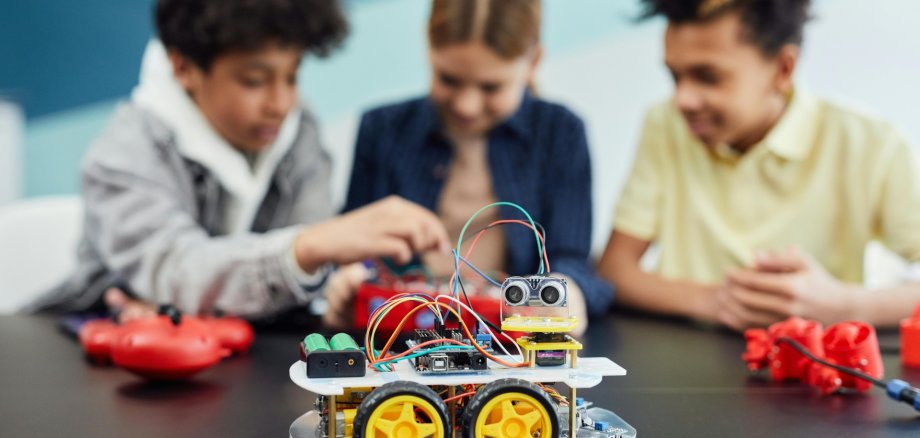 Drei Kinder an einem Tisch bauen miteinander einen Roboter, ein fertiger steht im Vordergrund