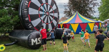 Riesengroße aufblasbare Dartscheibe und spielende Kinder auf der Aktionswiese