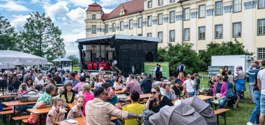 Festwiese mit vielen Menschen und Festbühne mit Schloss im Hintergrund