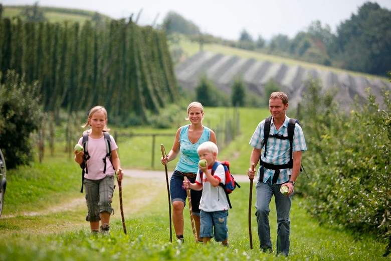 Vater, Mutter und 2 Kinder wandern durch Landschaft mit Hopfen und Obstbäumen