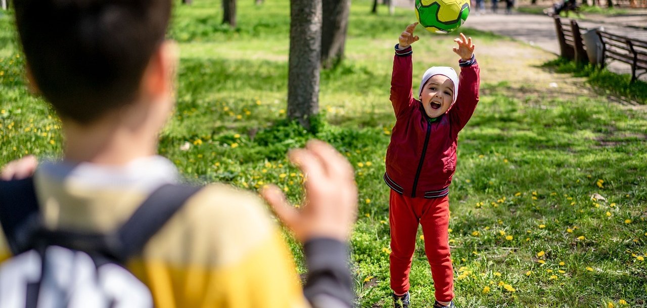 Junge wirft einen Ball zu anderem Jungen, der dem Betrachter den Rücken zukehrt