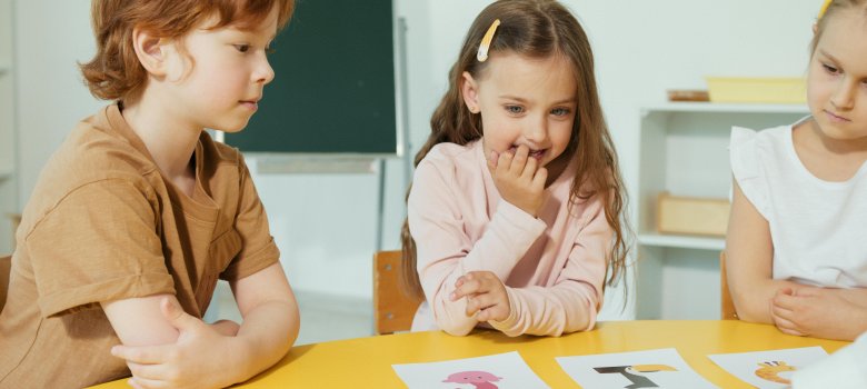 Ein Junge und zwei Mädchen im Grundschulalter sitzen an einem Tisch und betrachten Bilder