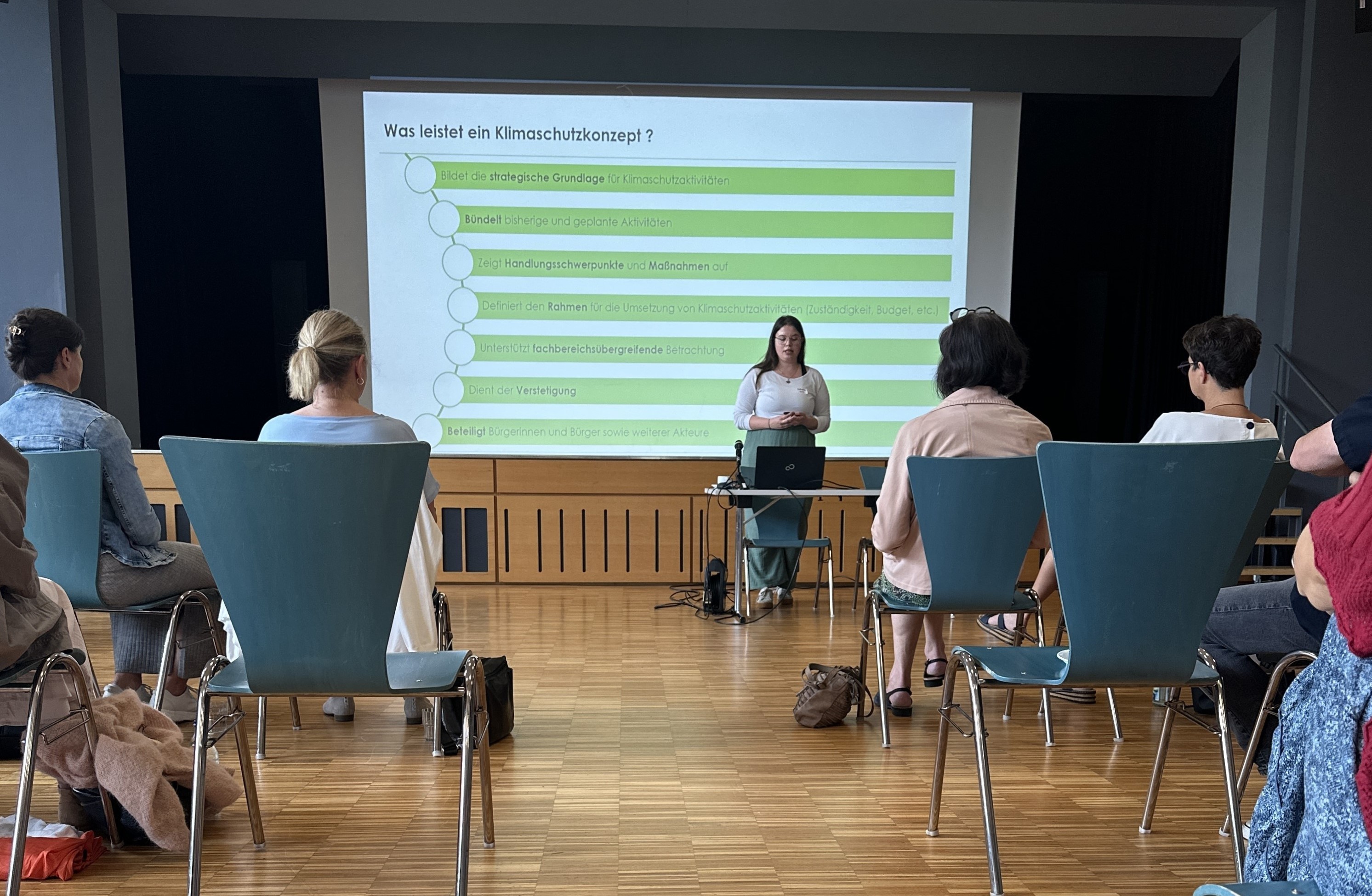 Klimaschutzmanagerin Katharina Kuhn hält einen Vortrag zum Klimaschutzkonzept (im Hintergrund die Präsentation auf einer Leinwand)