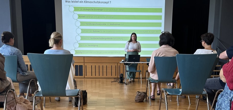 Klimaschutzmanagerin Katharina Kuhn hält einen Vortrag zum Klimaschutzkonzept (im Hintergrund die Präsentation auf einer Leinwand)