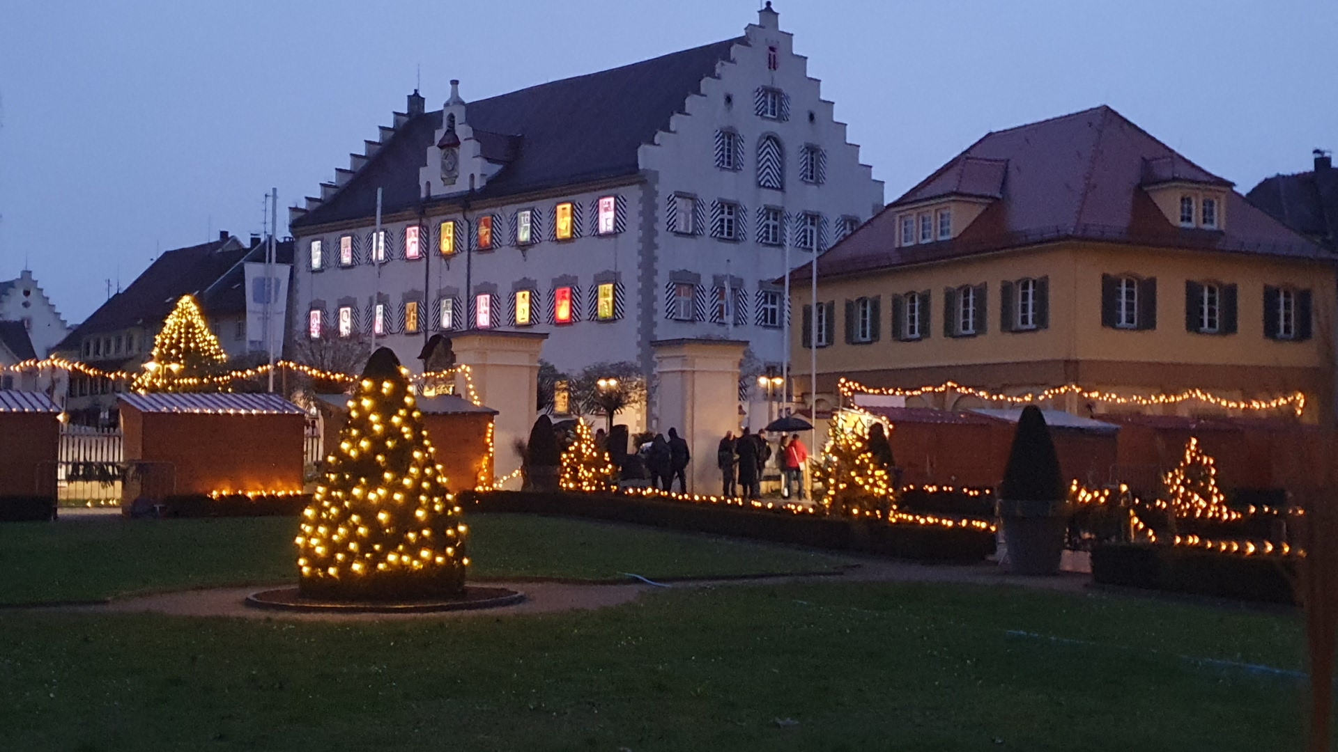 Rathaus und Kavaliersgebäude in der Dämmerung, weihnachtlich beleuchtet mit beleuchtetem Weihnachtsbaum im Vordergrund, vom Schloss aus gesehen