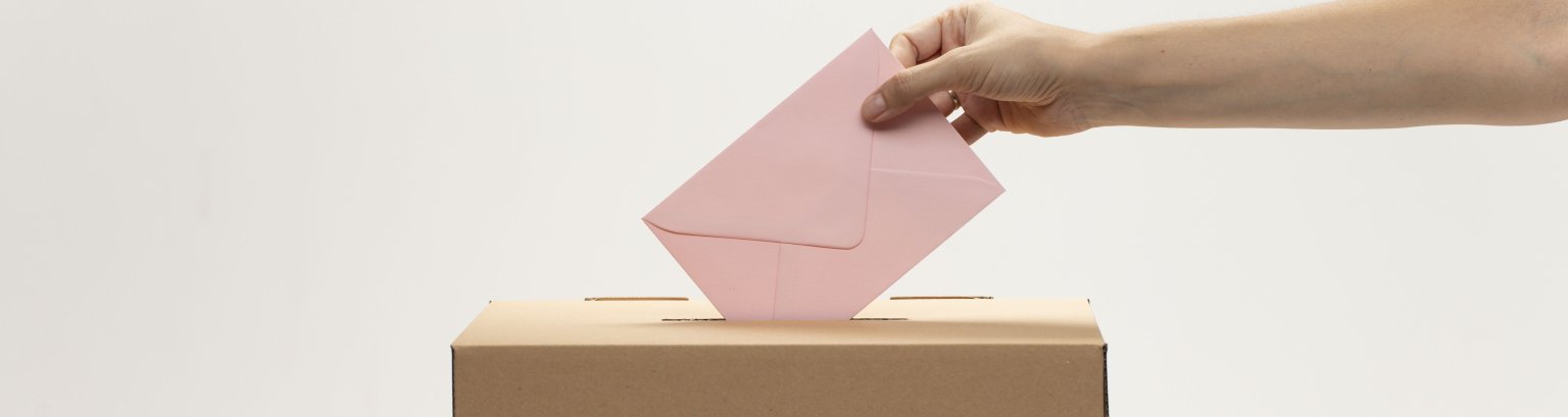 Hand wirft roten Umschlag in eine Wahlurne